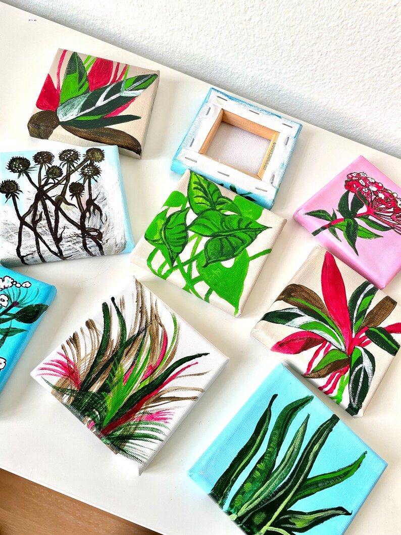 May include: Nine small canvas paintings with various botanical illustrations. The paintings feature different plants and flowers in shades of green, pink, red, and brown. The paintings are all on white canvases with a wooden frame.
