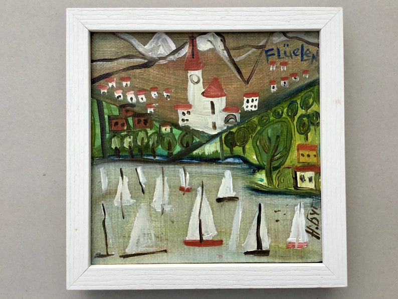 May include: A framed painting of a village with a church in the center, surrounded by green trees and white sailboats on a body of water. The painting is signed "H.B" and titled "Fl&uuml;elen".