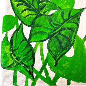 May include: A close-up of a painting on canvas featuring green leaves with a white background. The leaves are painted in a stylized manner, with thick strokes of green paint.