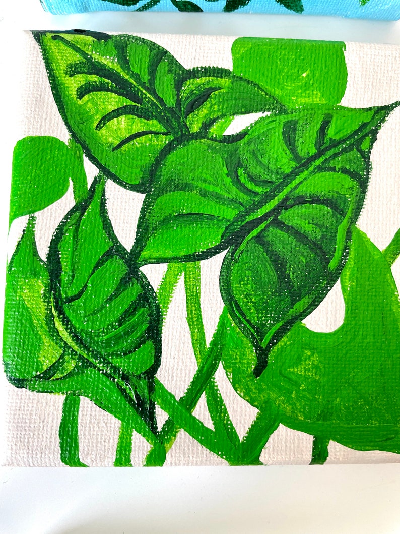 May include: A close-up of a painting on canvas featuring green leaves with a white background. The leaves are painted in a stylized manner, with thick strokes of green paint.