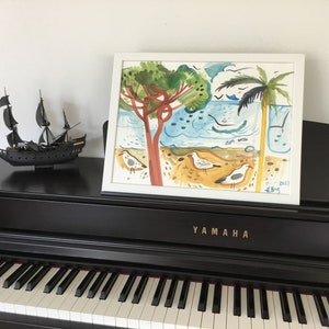 May include: A framed watercolor painting of a beach scene with palm trees, seagulls, and a blue ocean. The painting is on a black piano with a ship model in the foreground. The painting is signed and dated "13-1-2022 H.B.S."