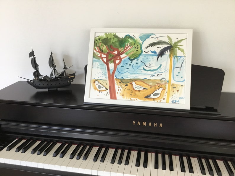 May include: A framed watercolor painting of a beach scene with palm trees, seagulls, and a blue ocean. The painting is on a black piano with a ship model in the foreground. The painting is signed and dated "13-1-2022 H.B.S."