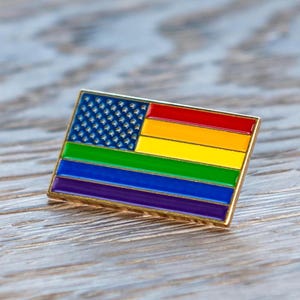 以下が含まれることがあります： 虹色のアメリカ国旗のデザインが施された金色のピン。旗は伝統的な星条旗ですが、ストライプは虹色です。