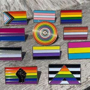 Peut inclure: Une collection de 12 épingles en émail représentant différents drapeaux de la fierté, notamment les drapeaux transgenre, bisexuel, lesbien, gay, pansexuel, asexuel, non-binaire et intersexué. Les épingles sont toutes dorées et ont un design arc-en-ciel.