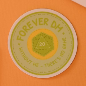 May include: A round sticker with the text "FOREVER DM" and "WITHOUT ME THERE'S NO GAME". The sticker has a green and yellow color scheme with a D20 die graphic in the center. Also visible are green push pins, a pen, and a notepad.