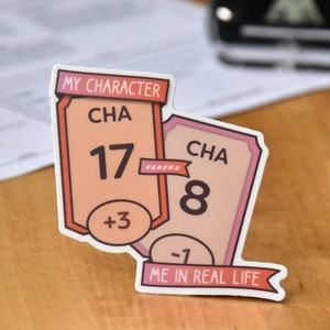 May include: Two pink and white stickers with the text "MY CHARACTER" and "ME IN REAL LIFE". The stickers are shaped like banners and have a number and a plus or minus sign on them. The text "CHA" is on both stickers. The number 17 with a plus 3 is on the top sticker. The number 8 with a minus 1 is on the bottom sticker. The text "VERSUS" is between the two stickers.