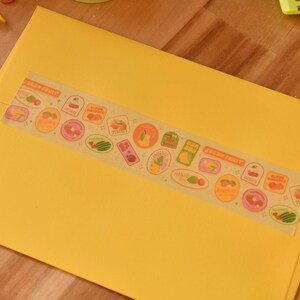 A yellow envelope is sealed with a piece of washi tape. The washi tape is a wide 30mm width featuring artwork of fruit stickers. The tape's label reads "Fruit Stickers Wide Washi Tape By Franki Hanke 30mm by 10M."