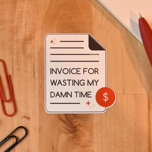 Op de afbeelding: Een sticker met de tekst "INVOICE FOR WASTING MY DAMN TIME" en een dollarteken. Een rode pen, een rode paperclip, een zwarte paperclip en een zwarte punaise zijn ook zichtbaar op een houten oppervlak.
