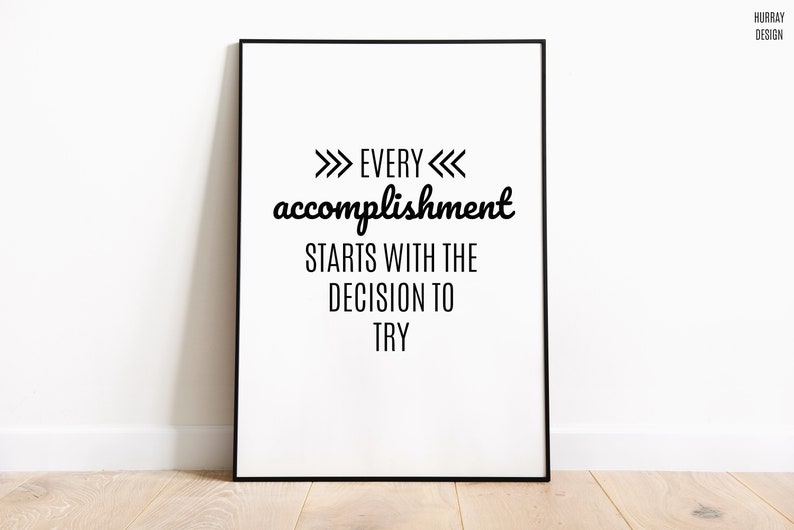 May include: Black and white motivational quote poster with the text "Every accomplishment starts with the decision to try" framed in a black frame.