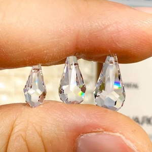 Puede incluir: Tres cuentas de cristal transparentes en forma de lágrima de diferentes tamaños, sostenidas en una mano. Las cuentas son facetadas y reflejan la luz.