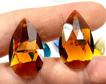 May include: Two amber teardrop-shaped crystal prisms with faceted edges. The prisms are held in a hand.