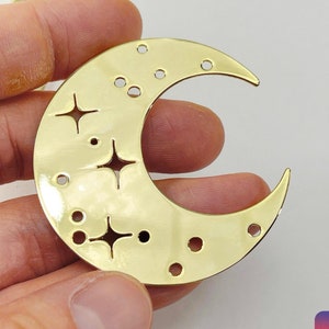Könnte beinhalten: Goldfarbener Metall-Halbmond-Anhänger mit einem ausgeschnittenen Design aus Sternen und Punkten. Der Anhänger hat Löcher zum Anbringen an Schmuck oder anderen Bastelarbeiten.