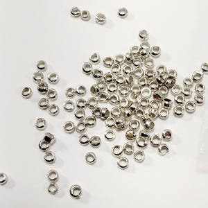 May include: A close-up image of a clear plastic bag filled with silver jump rings. The jump rings are scattered on a white surface. The image includes the text "Bitsy Supply" and a logo with the letter "B" in a rainbow design.