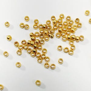 May include: A close-up of a bag of gold-colored metal beads. The beads are small and round, and they are scattered on a white surface. The bag is open, and the beads are spilling out.