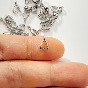 May include: A selection of small, silver-coloured bail connectors for jewellery making. The connectors are horseshoe-shaped with a small loop at the top for attaching to a chain. They are displayed on a white surface.