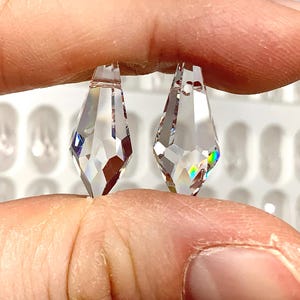 May include: Two clear crystal teardrop-shaped pendants, one slightly larger than the other, held in a hand.