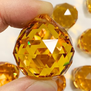 May include: A group of amber crystal ball ornaments with a faceted design. The ornaments are approximately 1 inch in diameter.
