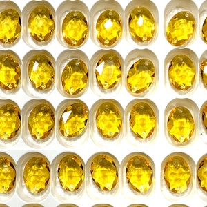 May include: A close-up view of a sheet of clear plastic packaging filled with small, round, yellow glass beads. The beads are arranged in rows and columns, and they are all the same size and shape.