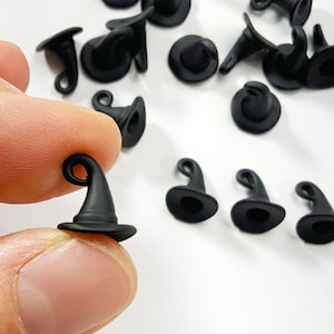 Pode incluir: Um grupo de 15 pingentes de chapéu de bruxa pretos. Os pingentes são pequenos e têm um laço na parte superior para pendurar. São perfeitos para adicionar um toque de fantasia às suas manualidades.