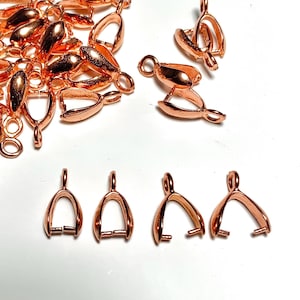 Op de afbeelding: Een verzameling koperkleurige sieradenonderdelen, waaronder karabijnsluitingen en hangerbeugels, ligt op een wit oppervlak. De sluitingen hebben een gebogen ontwerp, terwijl de beugels een lus hebben om aan een ketting of koord te bevestigen.