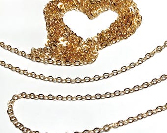 May include: A long gold chain made of small, linked circles. The chain is laid out in a heart shape and a long, flowing line.