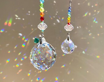 May include: Two hanging crystal suncatchers suspended from silver chains. Each features a vertical arrangement of small, multi-colored faceted beads in a rainbow sequence, accented by clear, cloud-shaped glass charms and large clear crystal prisms.