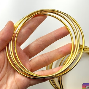 Pode incluir: Um conjunto de 10 argolas de metal dourado, empilhadas e seguradas em uma mão. As argolas são lisas e brilhantes.