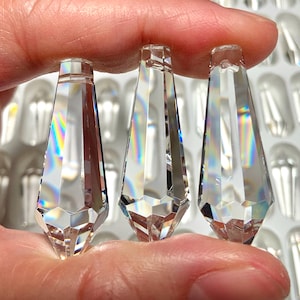 以下が含まれることがあります： ファセットカットされたエッジを持つ、透明なクリスタル製の涙型のペンダントが3つ。ペンダントは手で持たれています。