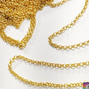 Puede incluir: Cadena de eslabones dorados, una opción popular para la elaboración de joyas, se muestra en una imagen de primer plano. La cadena está hecha de metal y tiene un acabado brillante. La cadena está dispuesta sobre una superficie blanca.