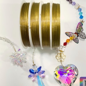 May include: Four spools of gold-colored wire for jewelry making, with a rainbow crystal suncatcher featuring a butterfly charm and a heart-shaped crystal pendant. The suncatcher is hanging from a gold-colored wire. Bitsy Supply is printed on the bottom of the image.