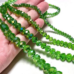 May include: Several strands of faceted, bright green beads of varying sizes. The beads have a sparkling, iridescent quality, reflecting light. The beads are displayed against a light background, showcasing their color and texture. These beads are suitable for jewelry making.
