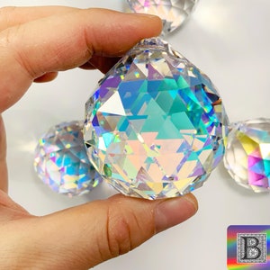 K&ouml;nnte beinhalten: Vier regenbogenfarbene Kristallkugeln, eine davon in der Hand gehalten, mit einem Regenbogeneffekt. Die Kugeln sind facettiert und haben eine klare, gl&auml;serne Optik.