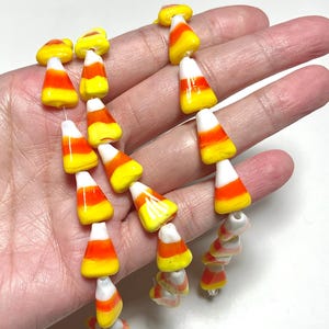 Könnte beinhalten: Eine Kette aus Candy-Corn-Perlen in Gelb, Orange und Weiß. Die Perlen sind aufgefädelt und bilden ein festliches und farbenfrohes Accessoire. Perfekt für Halloween oder Themenveranstaltungen.