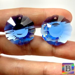 May include: Two blue crystal flower-shaped embellishments with a faceted design. The embellishments have two holes for hanging.