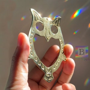 May include: A gold metal owl cutout with a heart-shaped opening. The owl has a detailed design with a decorative pattern around the edges.