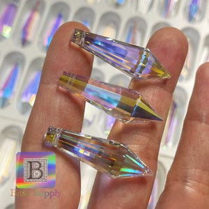 May include: Three iridescent crystal teardrop pendants with a pointed tip. The crystals are clear with rainbow-like reflections.