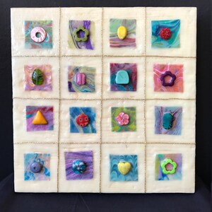 May include: A white square canvas with a grid of 16 squares. Each square contains a different colored background with a small, colorful, abstract shape in the center. The shapes include a circle, a flower, a lemon, a heart, a triangle, a star, and a teardrop.
