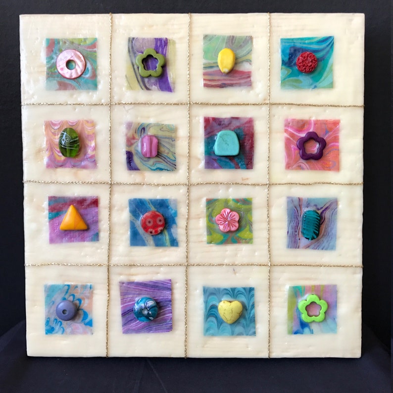 May include: A white square canvas with a grid of 16 squares. Each square contains a different colored background with a small, colorful, abstract shape in the center. The shapes include a circle, a flower, a lemon, a heart, a triangle, a star, and a teardrop.
