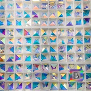 K&ouml;nnte beinhalten: Eine Nahaufnahme einer Folie mit irisierenden, facettierten, quadratischen Kristallen. Die Kristalle sind in einem Raster angeordnet und in verschiedenen Farben erh&auml;ltlich, darunter Blau, Lila und Pink.