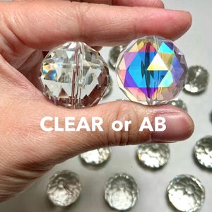 May include: Two round faceted crystal beads, one clear and one with an iridescent aurora borealis finish, featuring geometric cuts. The text CLEAR or AB is displayed across the center of the image, with additional clear beads scattered below.