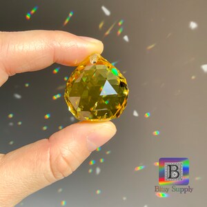 May include: A yellow crystal ball with many facets, creating rainbow reflections. The crystal is being held by a hand.