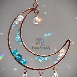 May include: Copper wire crescent moon with blue and clear crystal beads. The moon has a dangling crystal bead at the bottom.