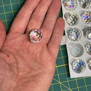 K&ouml;nnte beinhalten: Nahaufnahme einer klaren Kristallkugel mit Regenbogenfacetten. Die Kugel wird in einer Hand gehalten. Die Kugel ist Teil eines Sets von Kristallkugeln in einer wei&szlig;en Verpackung.