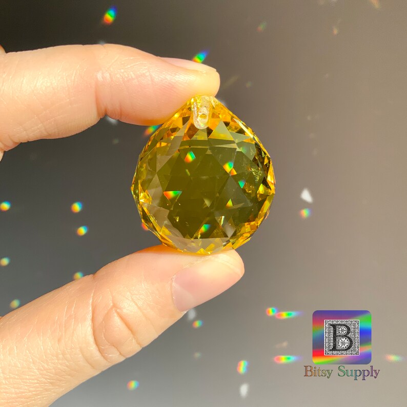 May include: A yellow crystal ball with a faceted design. The crystal is hanging from a silver loop.