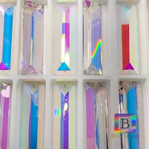 Peut inclure: Gros plan sur un plateau de pendentifs en verre prismatique iris&eacute;. Les prismes sont dispos&eacute;s en rang&eacute;es et sont de formes et de tailles diff&eacute;rentes. Les prismes r&eacute;fl&eacute;chissent la lumi&egrave;re et cr&eacute;ent un effet arc-en-ciel.
