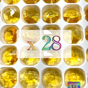 Puede incluir: Primer plano de 28 cuentas de vidrio &aacute;mbar de forma octogonal con un agujero en el centro. Las cuentas est&aacute;n dispuestas en una bandeja de pl&aacute;stico blanco con compartimentos individuales. El texto "X 28" est&aacute; impreso en colores arco&iacute;ris en el centro de la imagen.