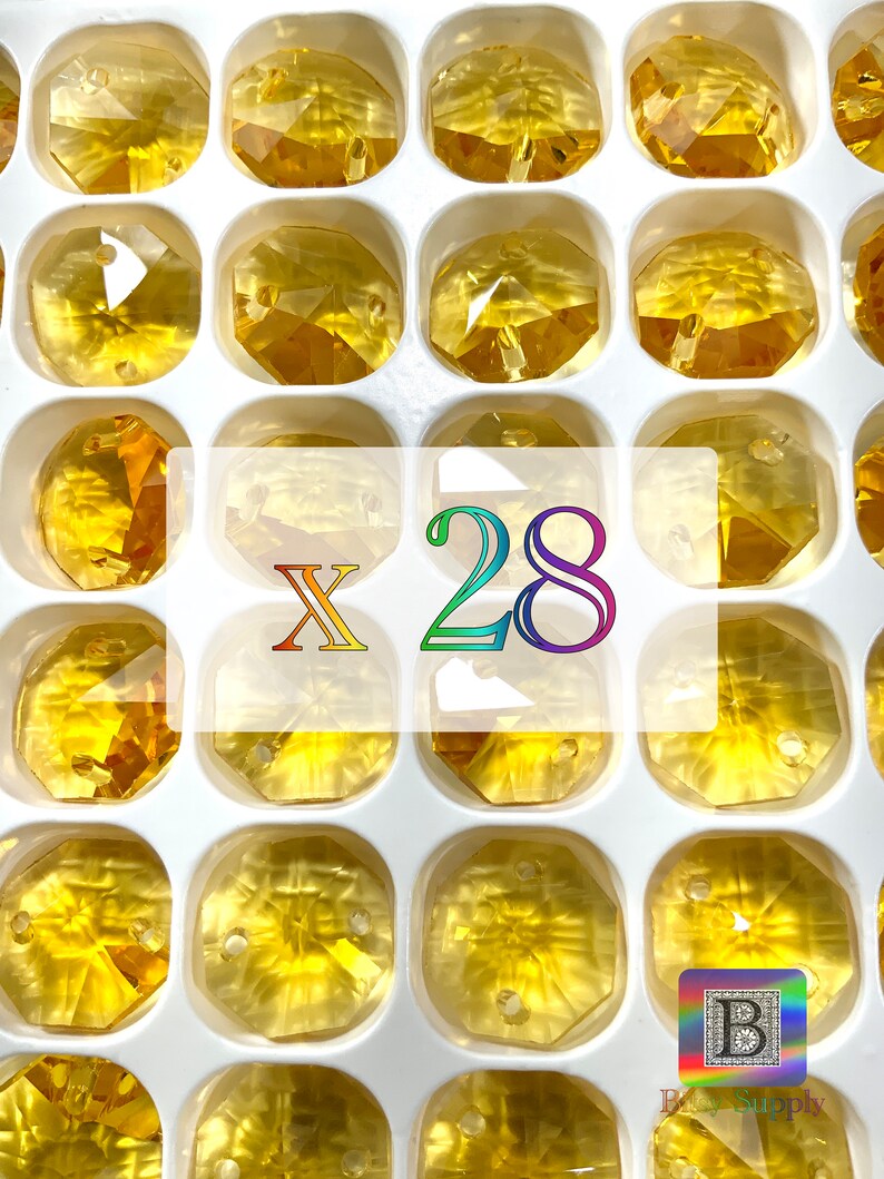 Puede incluir: Primer plano de 28 cuentas de vidrio &aacute;mbar de forma octogonal con un agujero en el centro. Las cuentas est&aacute;n dispuestas en una bandeja de pl&aacute;stico blanco con compartimentos individuales. El texto "X 28" est&aacute; impreso en colores arco&iacute;ris en el centro de la imagen.