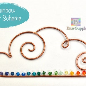 May include: A copper wire cloud with a rainbow of small glass beads. The cloud is made of wire that is bent into a cloud shape with a swirl on each side. The beads are arranged in a rainbow pattern along the bottom of the cloud. The text "Rainbow Color Scheme" is written in white on a blue oval above the cloud. The text "Bitsy Supply" is written in green below the cloud.