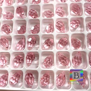 May include: A close-up view of a container filled with pink crystal teardrop shaped beads. The beads are arranged in rows and columns, and they are all the same size and shape.