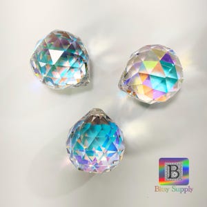 K&ouml;nnte beinhalten: Drei regenbogenfarbene Kristallkugeln mit facettierten Oberfl&auml;chen. Die Kugeln sind klar mit Regenbogenfarben, die von den Facetten reflektiert werden.